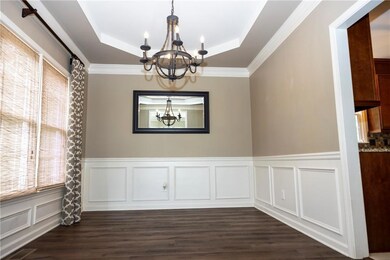 Dining area with a raised ceiling, a chandelier, dark wood-style floors, a wainscoted wall, and ornamental molding