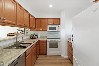 Kitchen featuring white appliances, brown cabinetry, light wood finished floors, light stone counters, and recessed lighting