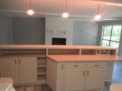 Kitchen with dark wood-type flooring, a brick fireplace, decorative light fixtures, white cabinetry, and light countertops