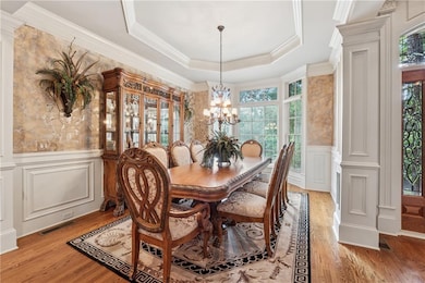 Dining room with a decorative wall, light wood finished floors, a chandelier, a wainscoted wall, and a tray ceiling