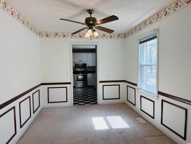 Spare room with a textured ceiling, visible vents, a decorative wall, a ceiling fan, and light carpet