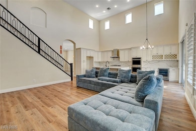 Living room featuring light wood-style flooring, beverage cooler, baseboards, recessed lighting, and a towering ceiling