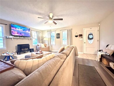 Living area with a textured ceiling, plenty of natural light, a ceiling fan, wood finished floors, and a fireplace with raised hearth