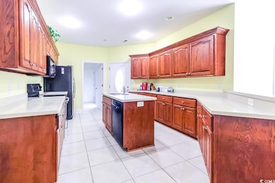Kitchen with a sink, black appliances, an island with sink, light countertops, and light tile patterned floors