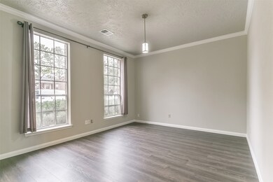 To the left of the foyer, a wide entrance opens into this spacious and inviting formal dining room with neutral grey paint, crisp white crown molding, a pendant light, wood-look laminate floors, and a pair of windows with front yard views.
