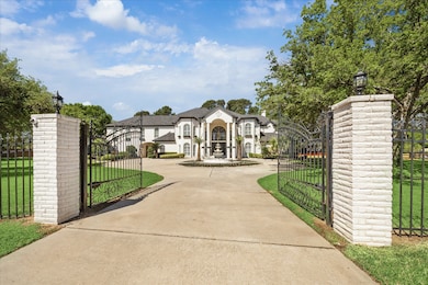 A grand two-story home with a gated entrance and circular driveway, featuring a central fountain. The exterior is elegant, surrounded by well-maintained lawns and mature trees, offering a luxurious and private ambiance.