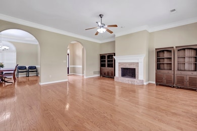 Unfurnished living room with arched walkways, a ceiling fan, a brick fireplace, crown molding, and light wood-style floors