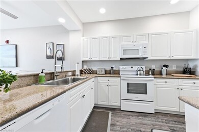 Kitchen with white appliances, light stone counters, white cabinets, dark wood-style flooring, and recessed lighting