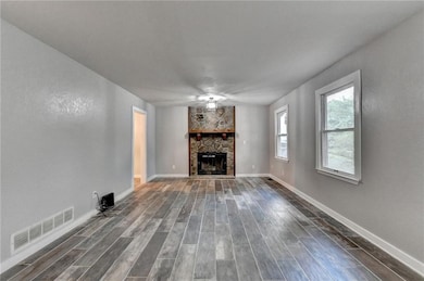 Unfurnished living room with a stone fireplace and dark wood finished floors