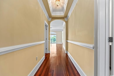 Hallway featuring arched walkways, crown molding, dark wood-style flooring, and a tray ceiling