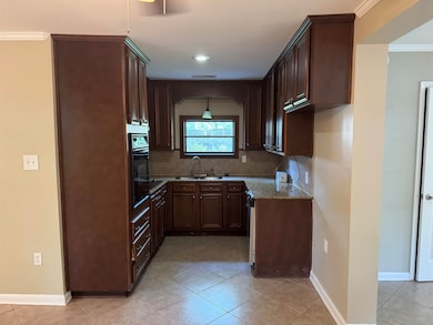 Kitchen with crown molding, backsplash, light tile patterned floors, dark stone counters, and dark brown cabinetry