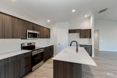 Kitchen with stainless steel appliances, light wood-style flooring, a kitchen island with sink, vaulted ceiling, and dark brown cabinetry