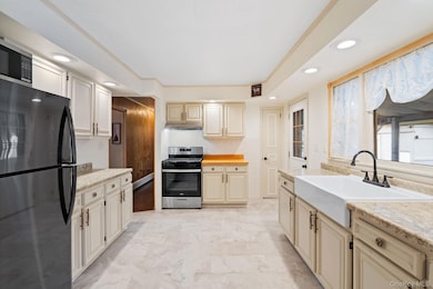 Kitchen featuring appliances with stainless steel finishes, cream cabinetry, recessed lighting, light stone counters, and baseboard heating