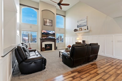 Carpeted living area featuring a decorative wall, a towering ceiling, a tiled fireplace, wainscoting, and a ceiling fan