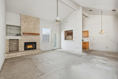 Unfurnished living room featuring carpet flooring, high vaulted ceiling, beam ceiling, a stone fireplace, and ceiling fan