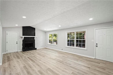 Unfurnished living room featuring light wood-style floors, lofted ceiling, a large fireplace, recessed lighting, and a textured ceiling