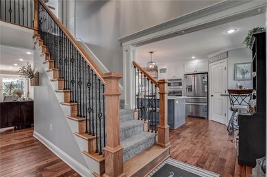 Stairway featuring hardwood / wood-style floors, ornamental molding, a chandelier, a high ceiling, and ornate columns