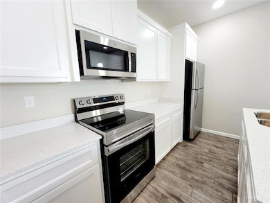 Kitchen with sink, stainless steel appliances, light stone counters, light hardwood / wood-style flooring, and white cabinets