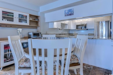 Kitchen featuring white cabinets, stainless steel appliances, open shelves, stone finish flooring, and dark stone counters