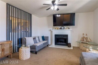 Carpeted living room with a ceiling fan and a fire