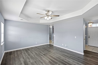 Unfurnished room featuring a raised ceiling, dark wood finished floors, and ceiling fan