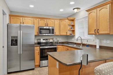 Kitchen with stainless steel appliances, open shelves, dark countertops, a peninsula, and light brown cabinets