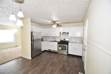 Kitchen featuring appliances with stainless steel finishes, white cabinets, pendant lighting, light countertops, and dark wood-style floors