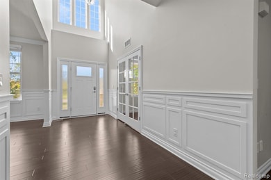Entrance foyer with a decorative wall, healthy amount of natural light, a wainscoted wall, dark wood finished floors, and a high ceiling