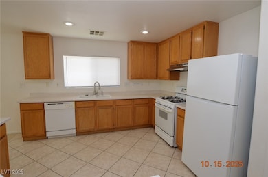 Kitchen with white appliances, light countertops, light tile patterned floors, under cabinet range hood, and recessed lighting