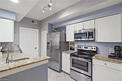 Kitchen with appliances with stainless steel finishes, a sink, white cabinetry, light stone countertops, and light tile patterned flooring