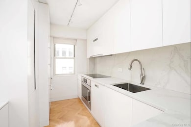 Kitchen featuring modern cabinets, white cabinetry, stainless steel oven, and tasteful backsplash