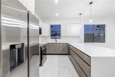 Kitchen with appliances with stainless steel finishes, modern cabinets, a peninsula, light marble finish flooring, and light countertops