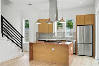 Kitchen with light stone counters, stainless steel appliances, hanging light fixtures, light wood finished floors, and recessed lighting