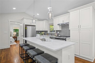 Kitchen featuring light stone countertops, vaulted ceiling, a breakfast bar, white cabinets, and dark wood-style flooring