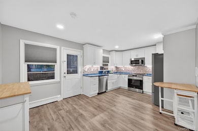 Kitchen with white cabinets, light wood-type flooring, decorative backsplash, appliances with stainless steel finishes, and baseboard heating