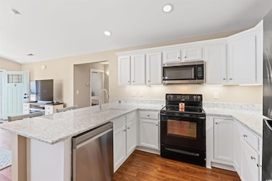 Kitchen with stainless steel appliances, white cabinets, dark wood-style floors, recessed lighting, and a peninsula