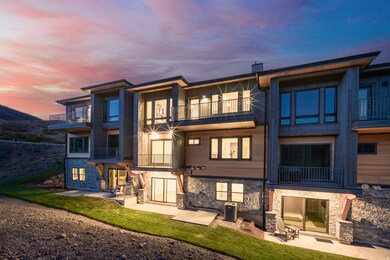 Rear view of property featuring a balcony, stone siding, a patio, a lawn, and a chimney