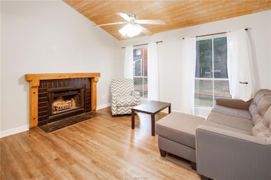 Living room featuring wooden ceiling, vaulted ceiling, light wood-type flooring, ceiling fan, and a brick fireplace