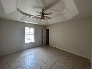 Empty room with a raised ceiling, ceiling fan, light tile patterned floors, and baseboards