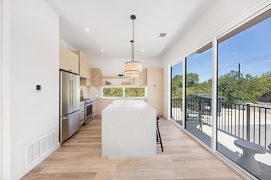 Kitchen with light brown cabinetry, modern cabinets, pendant lighting, light stone counters, and premium appliances