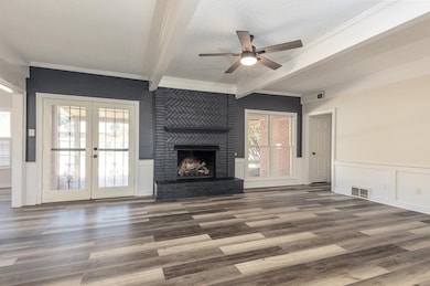 Unfurnished living room with a textured ceiling, a wainscoted wall, beam ceiling, ceiling fan, and a brick fireplace