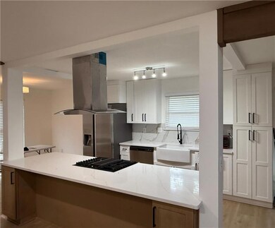 Kitchen featuring island exhaust hood, light stone counters, white cabinets, black appliances, and light wood-type flooring