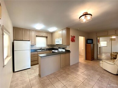 Kitchen with light tile patterned flooring, sink, light brown cabinets, kitchen peninsula, and white appliances