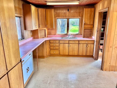 Kitchen featuring a sink, light countertops, brown cabinetry, wooden walls, and light floors