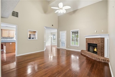 Unfurnished living room with high vaulted ceiling, dark wood-style floors, a brick fireplace, and a ceiling fan