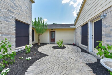 The courtyard is defined by a circular brick paver path leading to either the front door straight ahead or the game room door to the right. Mulched garden beds along the way are brightened by green foliage and brightly colored flowers.