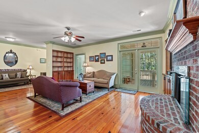 Living room with visible vents, crown molding, a brick fireplace, a ceiling fan, and wood-type flooring
