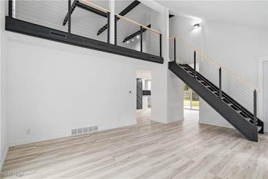 Unfurnished living room with high vaulted ceiling, light wood finished floors, and stairs