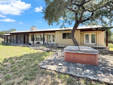 Back of property with french doors, a hot tub, a chimney, a metal roof, and a yard