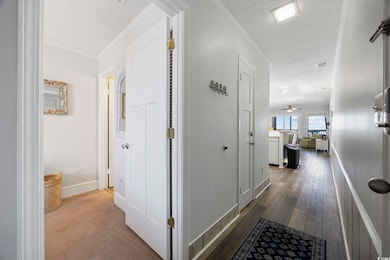 Hall featuring a textured ceiling, baseboards, ornamental molding, and dark wood finished floors